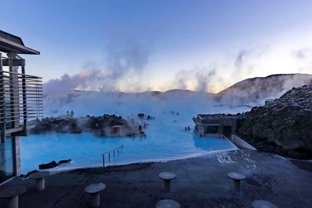 Iceland's famous Blue Lagoon with the natural steam raising to the sky, the bright blue water and the sun setting in the background.